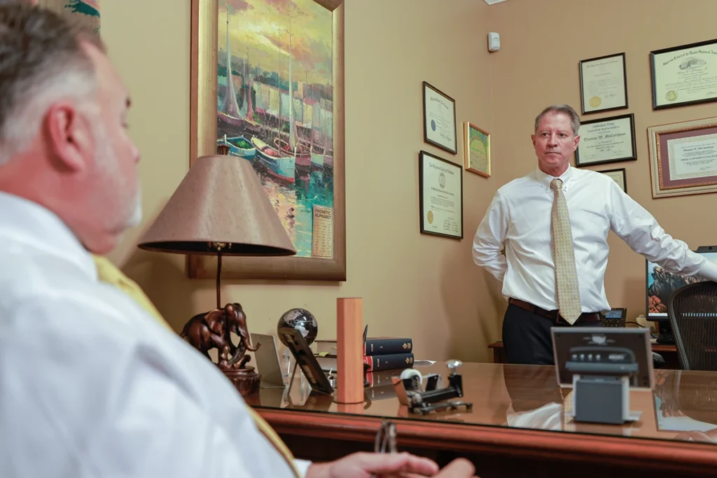 Joel Hamner and Tom McCutcheon discuss a car accident case with a client in an office filled with legal documents and decor.