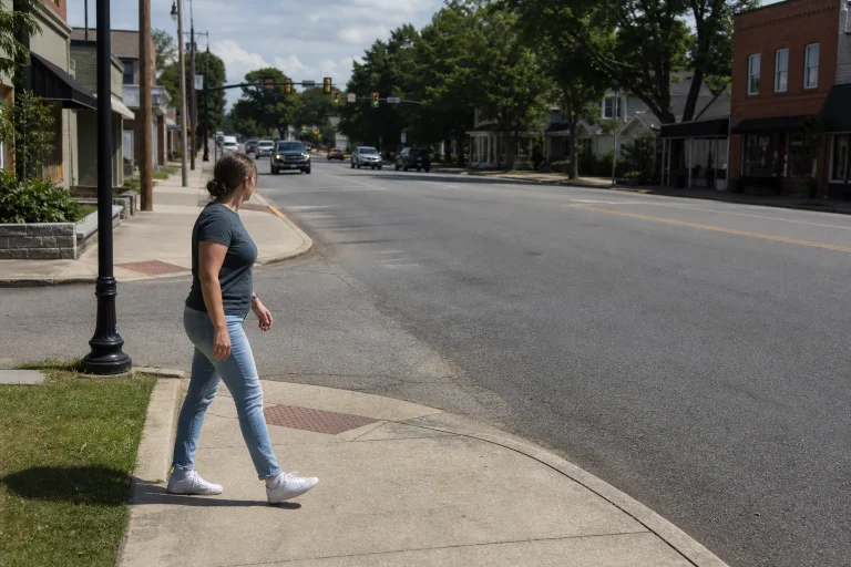 Pedestrian approaching an unmarked intersection crosswalk with visible sidewalks and roadway geometry