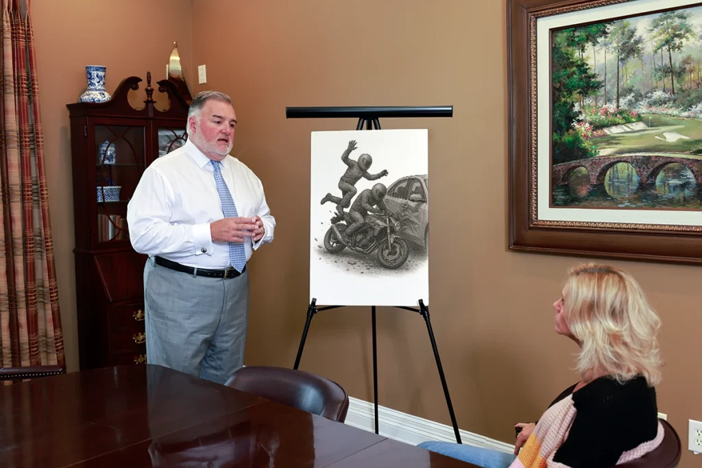 Attorney joel hamner explains a motorcycle passenger injury exhibit to a client, focusing on helmet damage analysis.