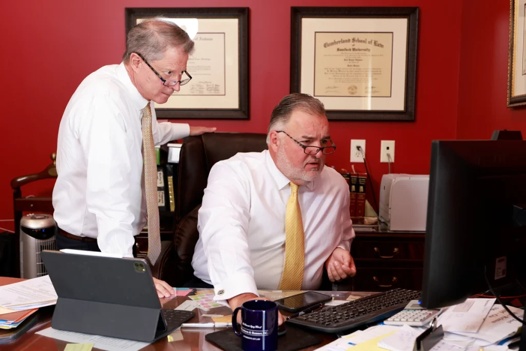 Tom and Joel, car accident lawyers, discuss a personal injury case at a desk filled with documents and a computer.