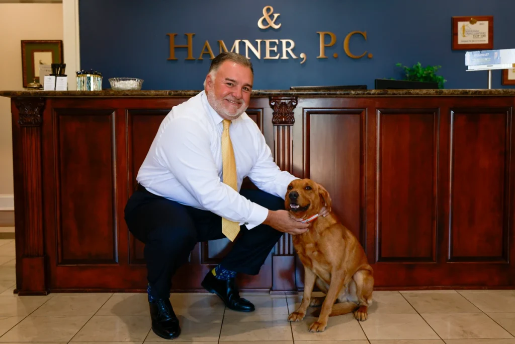 McCutcheon crouches beside a dog in front of a reception desk at McCutcheon & Hamner, P.C., both smiling at the camera.