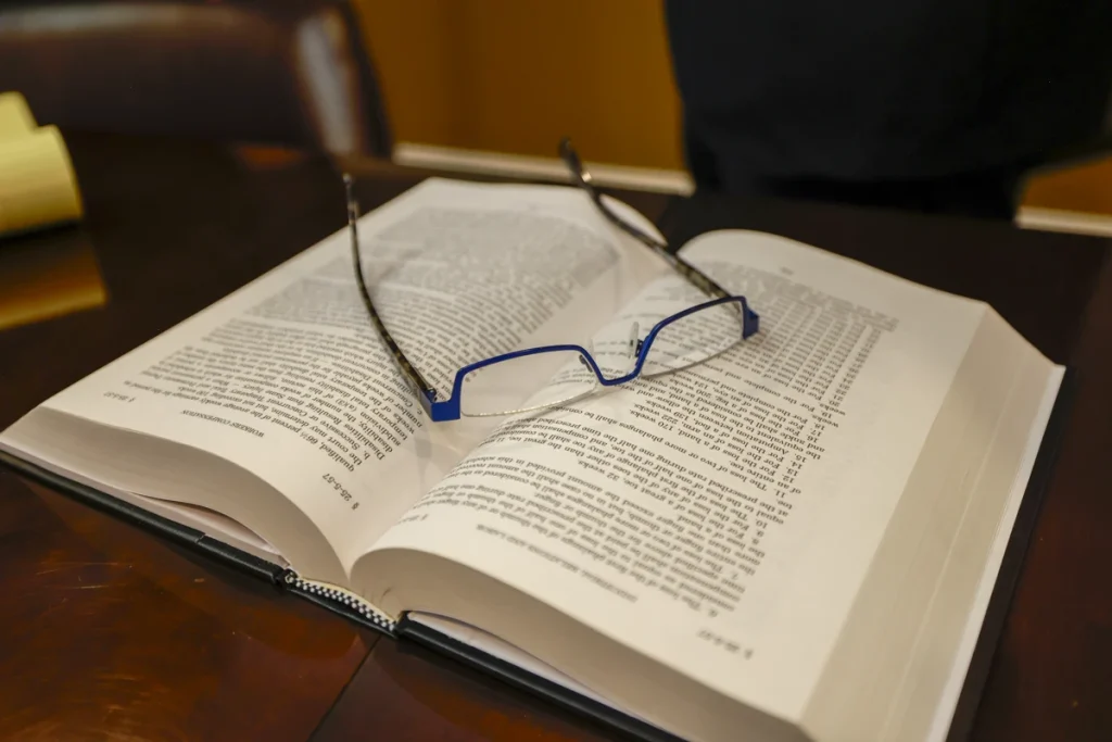 An open reference book titled "Alabama Statutes" with blue glasses resting on its pages, placed on a wooden table.