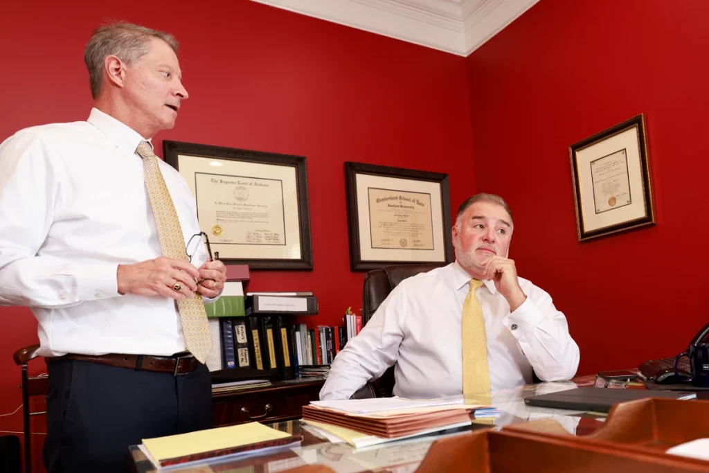 Tom and Joel discussing strategies for a personal injury case in a red-walled office with legal diplomas on the walls.